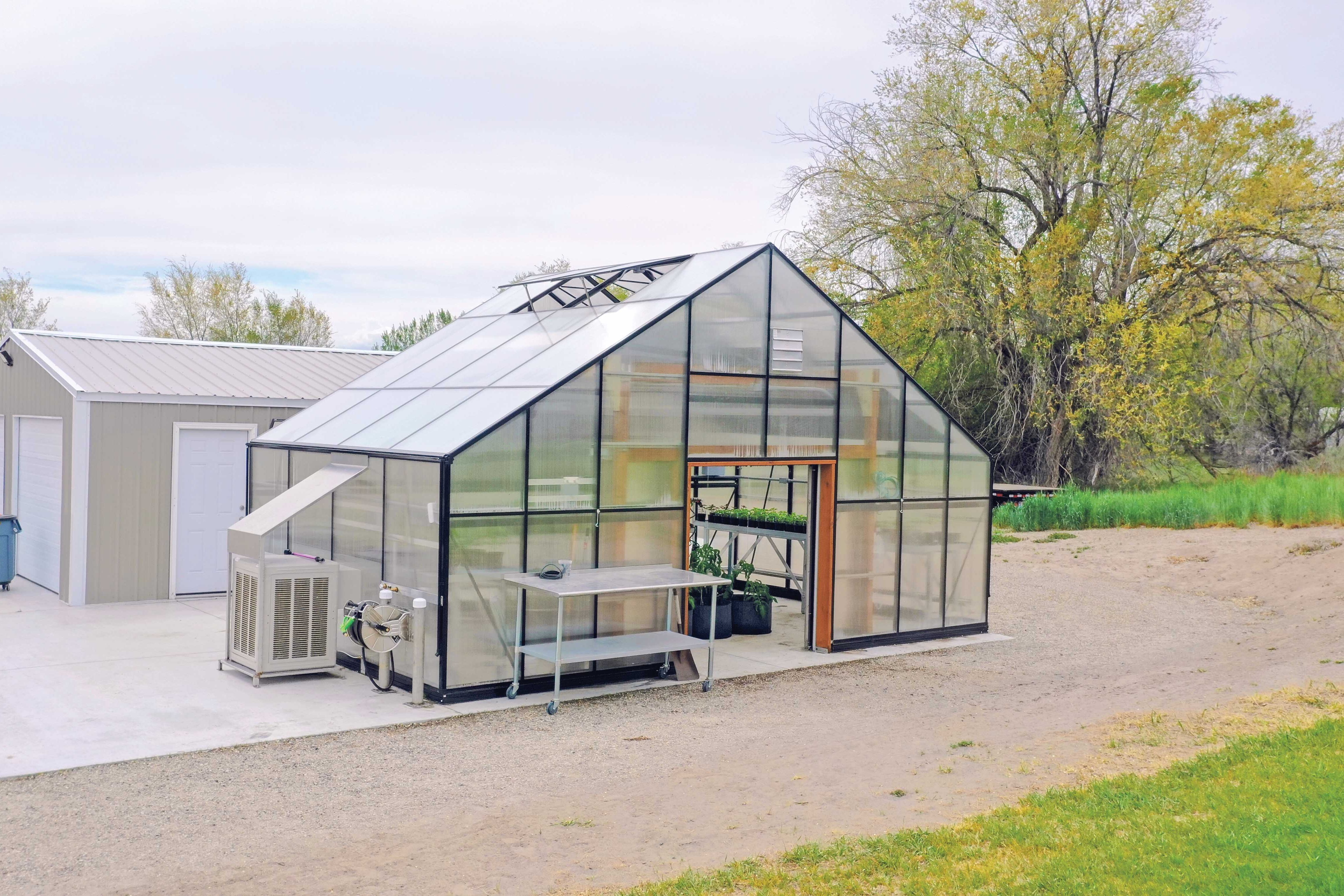 A GrowSpan Estate Deluxe Large Greenhouse in front of a metal headhouse