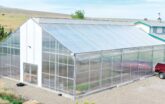 A GrowSpan Series 2000 Greenhouse with white polycarbonate on end wall, farmhouse in background